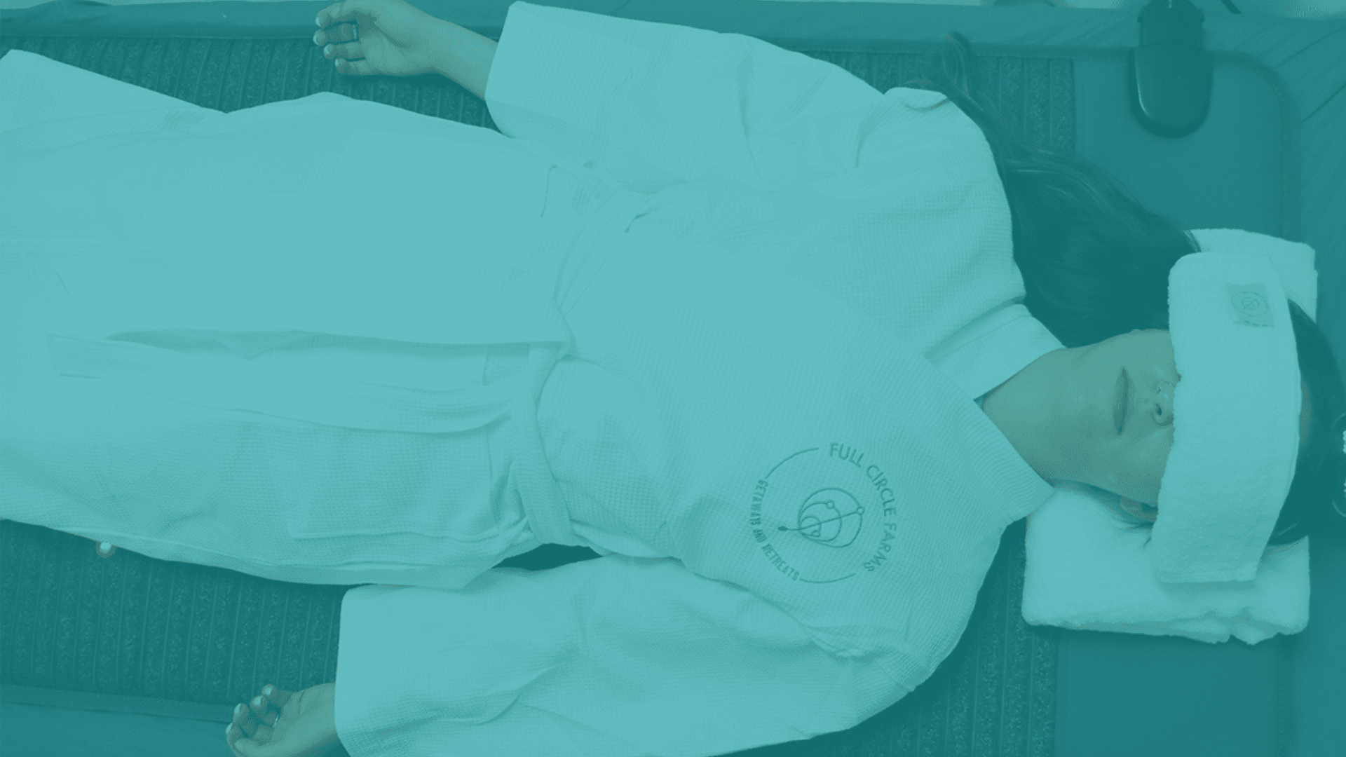 Person in a white spa robe with "Full Circle Farms" logo, a towel on their forehead, relaxing in a wellness setting.